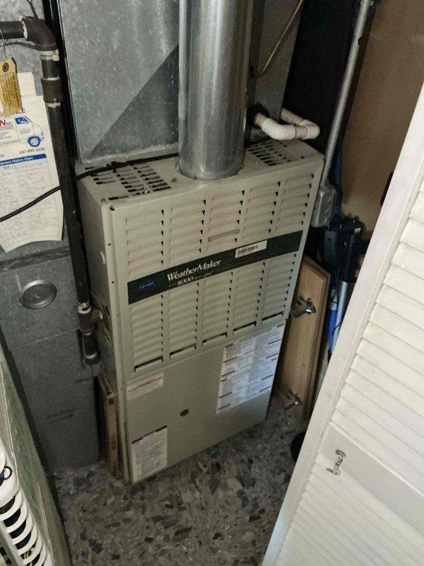 Evaluated existing HVAC system consisting of a 30+ year old Carrier WeatherMaker furnace and 10+ year old air conditioning unit in residential utility closet. Both systems currently operational but have exceeded their effective service life and require replacement. Inspected existing 1/4" refrigerant line set and determined complete replacement necessary due to age and improper sizing for new equipment installation. Noted drop ceiling configuration in installation area which will facilitate line set replacement process. Documented current equipment configuration including furnace unit, ductwork connections, water heater proximity, and electrical/refrigerant line routing. Photographed existing installation showing furnace with vertical duct extension, condensate drainage system, and mechanical room layout. Prepared comprehensive full system replacement estimate for new furnace and air conditioning unit with properly sized refrigerant lines to restore optimal heating and cooling efficien