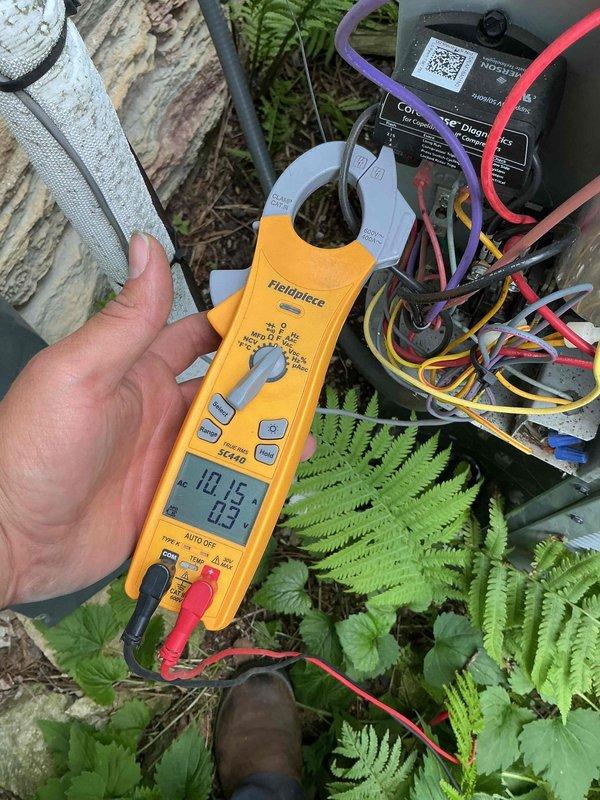 Performed comprehensive BFMA tune-up on 10+ year old residential air conditioning system. Removed condenser top panel to access and inspect internal components including fan assembly, electrical connections, and capacitor with visible wiring. Utilized Fieldpiece SC440 clamp meter to measure electrical parameters on refrigerant lines, recording readings of 10.15 and 0.3 to verify proper system operation and performance.