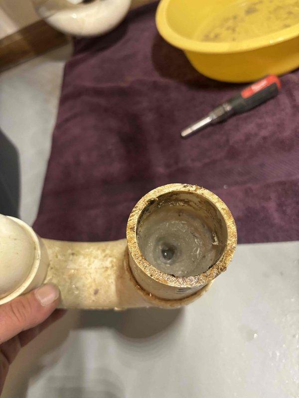 Responded to clogged floor drain service call. Upon arrival, accessed the drain plumbing beneath the fixture and removed the trap assembly to investigate the blockage. Inspection revealed significant mineral scale buildup and sediment accumulation inside the copper pipe fittings, which was restricting water flow and causing the drainage issue. Disassembled the affected plumbing components, cleared the blockage, and flushed the line to restore proper drainage. Reassembled all connections and verified system was draining freely with no leaks.