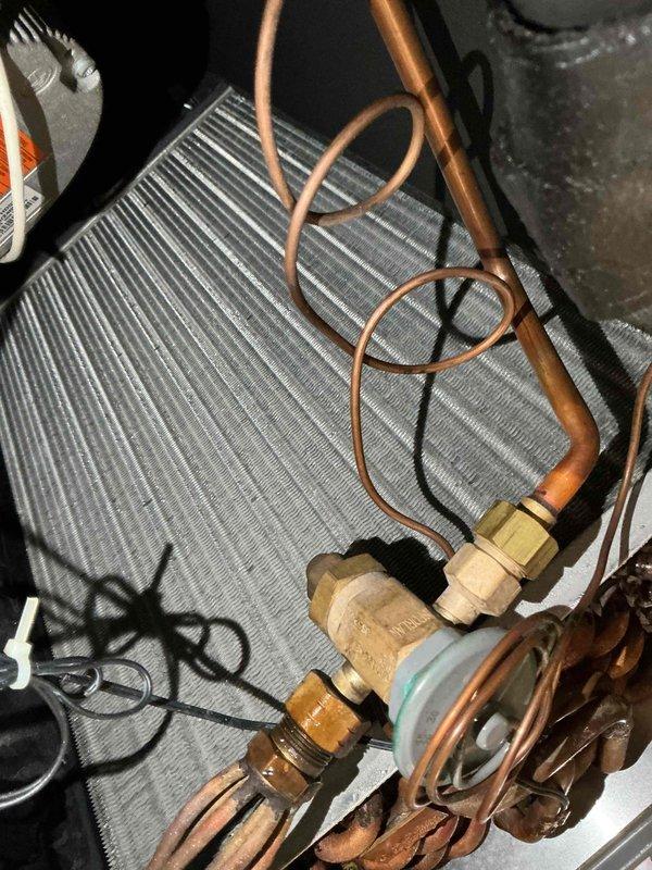 Completed comprehensive BFMA tune-up service on air handler system. Upon arrival, found outdoor condensing unit with significant debris accumulation including dried leaves and organic matter surrounding motor assembly and within equipment housing. Performed thorough cleaning of condenser unit, removing all debris from housing pan and around compressor motor. Inspected all electrical connections including motor wiring harness with red, white, and blue conductors. Evaluated heat exchanger coil fins and copper refrigerant lines for proper condition. Checked all brass fittings, valve connections, and refrigerant line connections at evaporator coil assembly. Verified system components operational and cleared all obstructions to ensure proper airflow and equipment function.