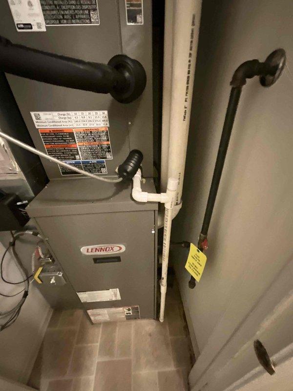 Completed installation of Lennox ML13KC1 air conditioning unit with matching cased evaporator coil in residential utility closet. Connected refrigerant lines, condensate drainage system via PVC piping, and electrical components including outdoor disconnect box. Reinstalled thermostat and verified system operation with existing Lennox furnace for proper heating and cooling integration.