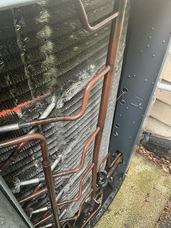 Completed comprehensive BFMA tune-up service on a 10-year-old outdoor air conditioning unit. Performed full system inspection including condenser coil examination, refrigerant line assessment, and verification of unit operation. Observed frost accumulation on evaporator coil fins indicating potential airflow restriction or refrigerant charge concerns; documented copper refrigerant tubing showing normal oxidation consistent with outdoor exposure. Verified unit is positioned on stable concrete pad with adequate clearance from surrounding landscaping including vine growth and evergreen shrubs. All maintenance procedures completed per BFMA standards with system operational at time of departure.