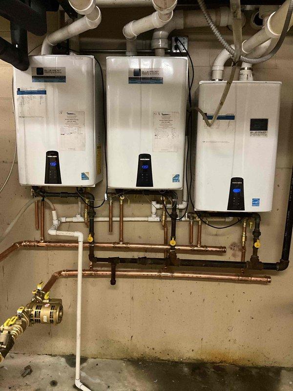 Completed re-piping of the plumbing manifold system servicing three Navien tankless water heaters and storage tank in a multi-unit building. Removed and replaced all copper supply piping and manifold connections linking the three wall-mounted units. Installed new copper pipe runs with proper horizontal configuration, incorporating yellow-handled shut-off valves at strategic points throughout the system for individual unit isolation and maintenance access. 

Replaced brass manifold fittings and valve assemblies to ensure proper flow distribution across all three heating units. Integrated white PVC drainage piping with existing system while maintaining proper venting requirements for each tankless unit. Verified all PVC vent pipes were properly routed through ceiling penetrations with appropriate clearances.

Connected flexible gas supply line with brass shut-off valve to maintain safe fuel delivery to the heating system. Ensured all copper joints were properly soldered and pressure-test