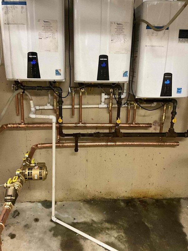 Completed re-piping of the plumbing manifold system servicing three Navien tankless water heaters and storage tank in a multi-unit building. Removed and replaced all copper supply piping and manifold connections linking the three wall-mounted units. Installed new copper pipe runs with proper horizontal configuration, incorporating yellow-handled shut-off valves at strategic points throughout the system for individual unit isolation and maintenance access. 

Replaced brass manifold fittings and valve assemblies to ensure proper flow distribution across all three heating units. Integrated white PVC drainage piping with existing system while maintaining proper venting requirements for each tankless unit. Verified all PVC vent pipes were properly routed through ceiling penetrations with appropriate clearances.

Connected flexible gas supply line with brass shut-off valve to maintain safe fuel delivery to the heating system. Ensured all copper joints were properly soldered and pressure-test
