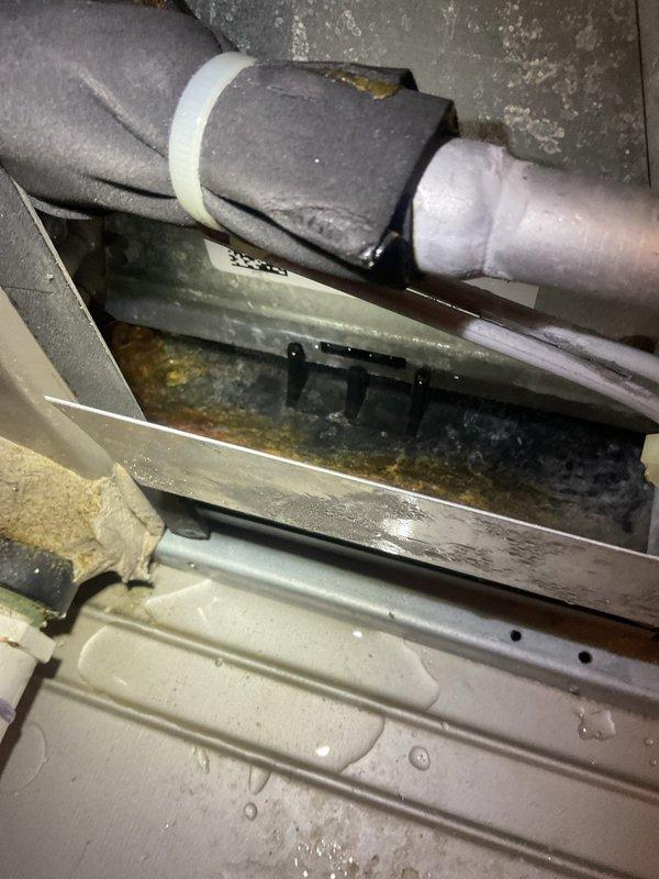 Responded to after hours call for water leaking from 5-year-old air conditioning system. Upon inspection, found standing water with visible discoloration and debris accumulation in condensate drip pan beneath air handler unit. Identified clogged condensate drain line as source of leak, preventing proper drainage from evaporator coil during cooling operation.