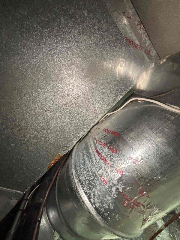 # No Cool Service Call

Responded to no cooling complaint affecting entire home. Upon inspection, discovered significant ice buildup on supply ductwork and evaporator coil section, indicating restricted airflow or low refrigerant charge. Observed rust and corrosion on interior components near condensate area, suggesting possible moisture intrusion or drainage issues. 

Documented frozen ductwork with heavy frost accumulation on metal surfaces and elbow joints. System shutdown required to allow ice to thaw before further diagnostics could be performed. Recommended follow-up inspection after thaw cycle to check refrigerant levels, airflow restrictions, filter condition, and blower motor operation to determine root cause of freezing condition.