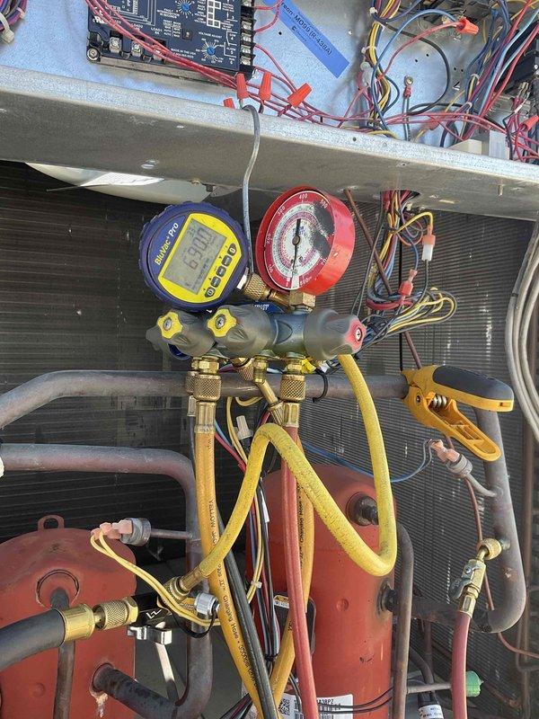 Performed commercial RTU repair with parts and refrigerant staged from headquarters. Replaced heavily corroded and rusted exterior panel showing extensive weathering damage with vertical streaking patterns. Connected manifold gauge set to system and performed refrigerant charging procedures using Yellow Jacket diagnostic equipment, monitoring pressures on both high and low side gauges to verify proper system operation and refrigerant levels.