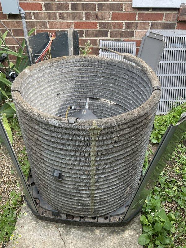 Completed comprehensive BFMA tune-up on outdoor air conditioning condenser unit aged 6+ years. Removed protective cover to access cylindrical condenser coil assembly, which exhibited heavy accumulation of dirt, debris, dust, and organic matter including moss and algae growth along the upper rim and throughout the fin surfaces. Performed thorough cleaning of condenser coils to restore proper airflow and heat transfer efficiency, addressing significant buildup that had accumulated from extended outdoor service exposure. Inspected electrical components, wiring, and internal connections for proper operation. Reassembled unit and verified system performance upon completion of maintenance service.