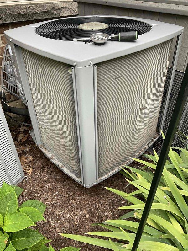 Completed comprehensive BFMA tune-up service on two outdoor air conditioning condensing units at residential property. Performed standard preventive maintenance procedures including inspection of condenser coils, verification of proper airflow through louvered panels, examination of electrical connections and capacitor, and assessment of fan operation. Both units showed good operational condition with protective mesh screens intact and equipment properly maintained on mulched ground surface.