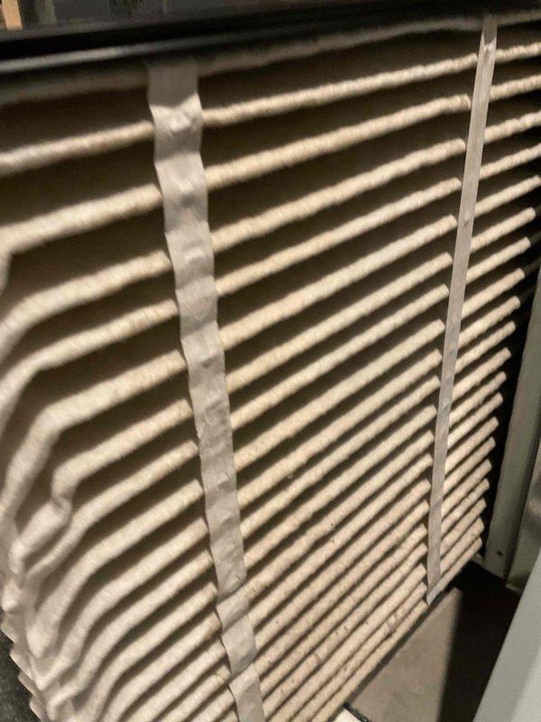 Completed comprehensive AC tune-up on 7+ year old system. Inspected and photographed air filter showing clean condition with intact pleated media and proper frame structure. Performed exterior condenser unit inspection, revealing coil assembly with visible debris accumulation and white buildup on fins, along with signs of weathering and discoloration between fin sections. System evaluated for operational performance and maintenance requirements.