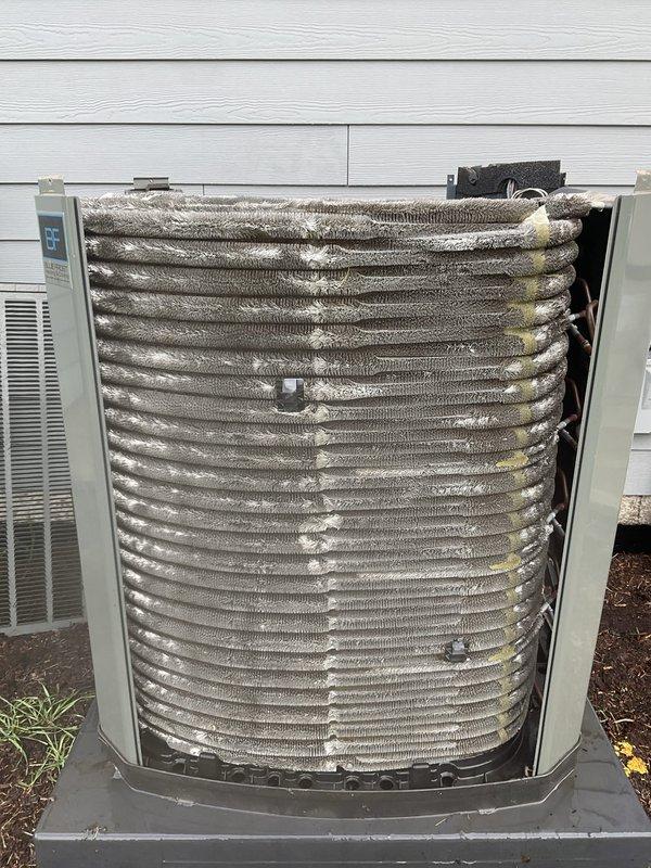 Completed comprehensive AC tune-up on 7+ year old system. Inspected and photographed air filter showing clean condition with intact pleated media and proper frame structure. Performed exterior condenser unit inspection, revealing coil assembly with visible debris accumulation and white buildup on fins, along with signs of weathering and discoloration between fin sections. System evaluated for operational performance and maintenance requirements.