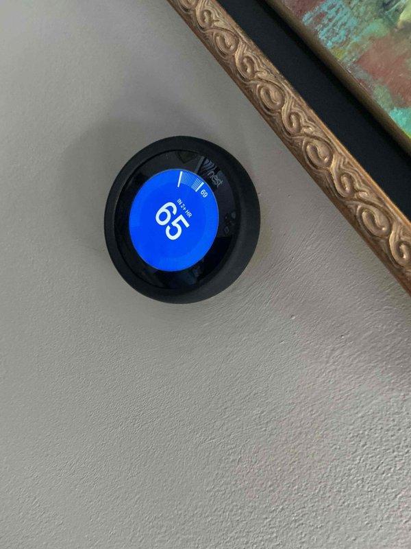 Completed comprehensive BFMA tune-up service on a 7+ year old residential air conditioning system. Performed full system inspection of outdoor condenser unit, which showed signs of age-related weathering and rust staining on exterior panels. Verified thermostat operation with Nest unit displaying proper temperature control at 65 degrees. Inspected condenser coils through protective grilles, checked fan motor assembly and grille components, and evaluated overall unit performance to ensure optimal cooling efficiency for continued operation.