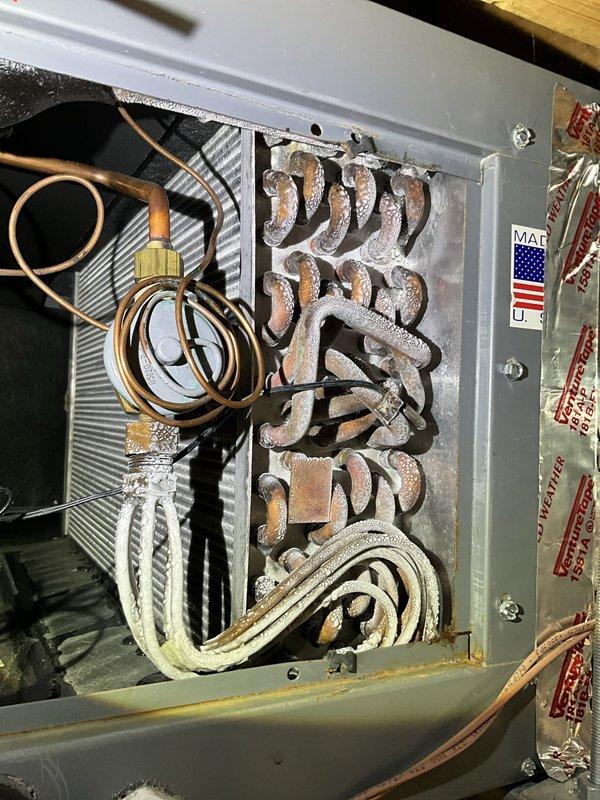 Responded to service call for thermostat continuously rebooting during air conditioning operation. Previous surge protector installation did not resolve the issue. Performed comprehensive electrical diagnostics using multimeter, measuring 12.14 volts at critical system components. Upon inspection, discovered severely corroded evaporator coil with extensive white and gray mineral buildup throughout the heating element assembly. Corrosion had compromised system integrity, causing electrical irregularities that triggered thermostat reboot cycles specifically during cooling mode operation. Documented coil deterioration with photographic evidence showing chalky deposits on serpentine coils and connected refrigerant lines. Determined that electrical instability was caused by failing evaporator coil rather than power supply issues. Recommended and sold evaporator coil replacement to resolve intermittent thermostat malfunction and restore proper system operation.