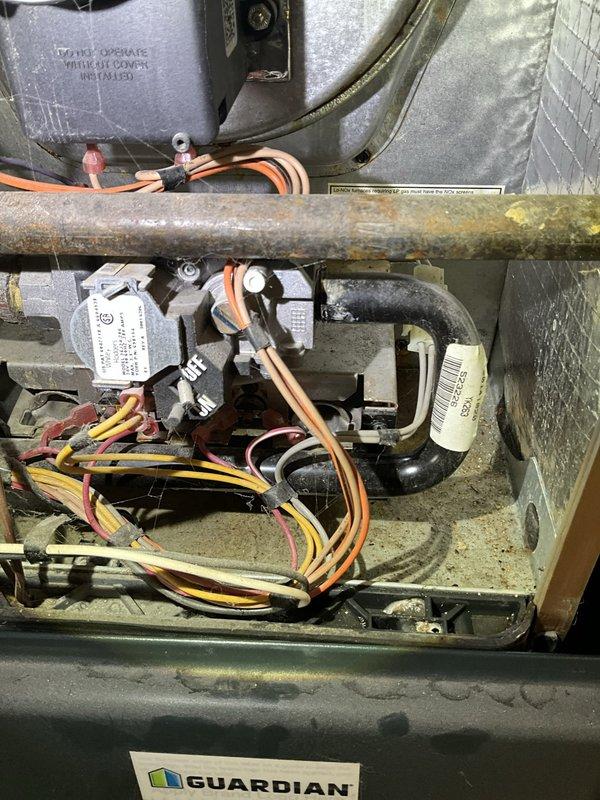 Responded to no cooling call on 15+ year old residential HVAC system with reported water leak of unknown origin. Upon inspection, discovered significant corrosion on refrigerant lines and internal piping within the air handler compartment, with rust and yellowish deposits indicating long-term moisture exposure. Traced water leak source to drain system issues, evidenced by PVC drainage components in mechanical area showing signs of improper pitch or blockage. Documented equipment condition including Guardian-branded unit with aged internal components, corroded piping, and compromised insulation. Recommended system evaluation for refrigerant line integrity and complete drain line service to address both cooling failure and active water leak.