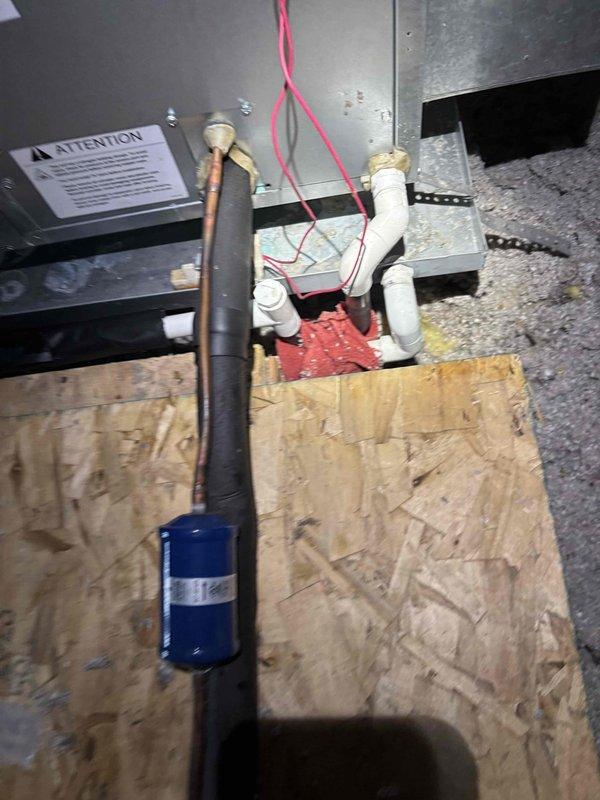 Completed A/C tune-up service for non-member system located in attic space. Upon inspection, identified significant crack in ceiling directly below air handler installation point. Documented existing condensate drain assembly showing corroded metal pipe section within P-trap configuration, which exhibited moisture accumulation and oxidation. Photographed HVAC equipment installation including filter drier, refrigerant lines with pink electrical wiring, and PVC condensate piping mounted on plywood platform. Verified attic access is safe with adequate structural beam support for service access. Customer advised to contact for follow-up regarding ceiling damage assessment.