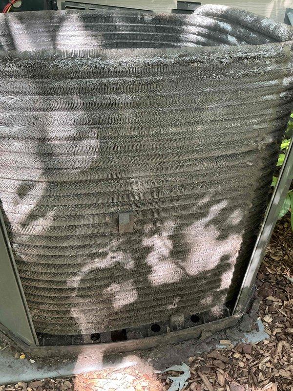 Completed comprehensive BFMA tune-up service on 9+ year old outdoor air conditioning condenser unit during afternoon appointment window. Performed standard AC maintenance protocol including inspection of cylindrical condenser unit with horizontal fin assembly, evaluation of coil condition which showed moderate accumulation of dirt, debris, and environmental particulates between fins, and assessment of unit mounted on concrete pad with mulch landscaping. All components inspected and serviced per manufacturer specifications to ensure optimal system performance for the cooling season.