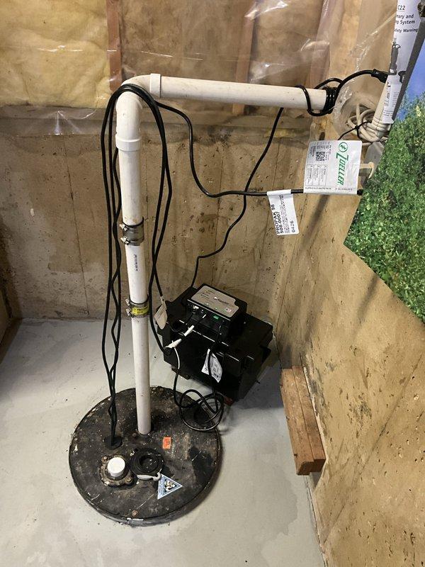 Installed a complete Zoeller drop-in sump pump system featuring both primary and backup pumps in basement sump basin. System includes white PVC vertical discharge piping with horizontal run secured to foundation wall, black electrical connections to backup battery unit, and all necessary mounting hardware. All components installed per manufacturer specifications with warranty coverage provided on pumps, charger, battery, and labor.