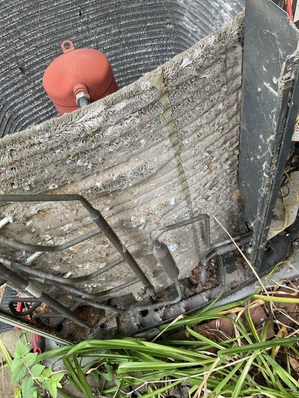 Completed comprehensive BFMA tune-up service on 14+ year old outdoor air conditioning condenser unit. Upon arrival, unit exhibited extensive dirt accumulation, algae growth, and debris buildup on exterior casing and coil fins, with heavy mineral deposits and frost formation affecting heat transfer efficiency. Performed thorough coil cleaning to remove organic matter and encrusted buildup from fin surfaces, cleared vegetation and leaf litter from base and perimeter area, inspected refrigerant lines and electrical connections for proper operation, and verified compressor assembly function. Unit restored to optimal operating condition with improved airflow and heat exchange capacity.