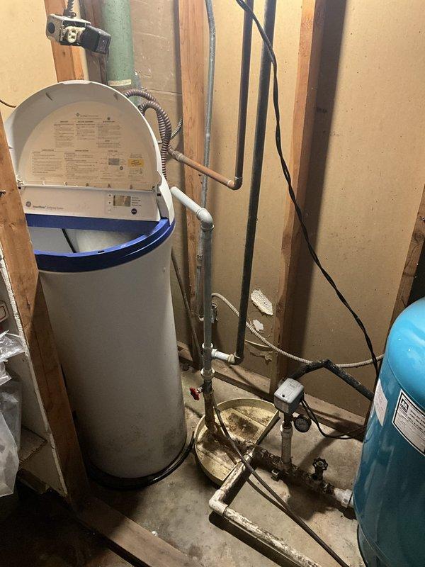 Responded to service call regarding black water discharge from well water system following water heater installation completed one year prior. Upon arrival, inspected tanked water heater installation and associated plumbing connections. Observed greasy residue on flex connectors and investigated potential contamination source affecting water quality. Examined sump pump system, pressure tank, and water heater configuration to identify cause of discoloration. Documented existing conditions including water heater with proper venting, blue pressure tank, plumbing connections, and sump pit installation with discharge piping. Assessed overall system operation and water flow characteristics to determine if issue originates from well system, sediment accumulation, or plumbing component degradation.