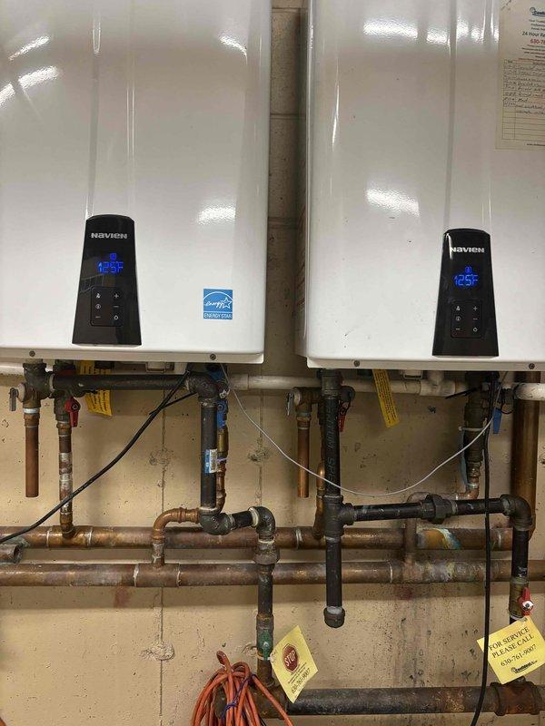Responded to service call regarding lukewarm water complaints from multiple unit owners in residential building. Upon arrival, inspected the water heating system which consists of two Navien tankless water heaters mounted in parallel configuration alongside a traditional storage tank water heater. 

Performed diagnostic testing on both tankless units, verifying digital display readings showing 125°F setpoint temperatures on control panels. Checked all incoming and outgoing water connections, including copper supply lines and distribution piping. Inspected pressure relief valves, shut-off valves, and pressure gauges throughout the system for proper operation.

Evaluated the traditional storage tank water heater for adequate heating capacity and proper function. Examined expansion tank mounting and pressure settings. Verified gas supply lines, venting system consisting of white PVC exhaust pipes, and all associated plumbing connections for code compliance and proper installation.

Tested