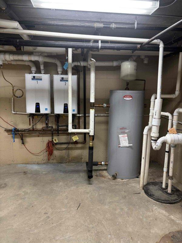 Responded to service call regarding lukewarm water complaints from multiple unit owners in residential building. Upon arrival, inspected the water heating system which consists of two Navien tankless water heaters mounted in parallel configuration alongside a traditional storage tank water heater. 

Performed diagnostic testing on both tankless units, verifying digital display readings showing 125°F setpoint temperatures on control panels. Checked all incoming and outgoing water connections, including copper supply lines and distribution piping. Inspected pressure relief valves, shut-off valves, and pressure gauges throughout the system for proper operation.

Evaluated the traditional storage tank water heater for adequate heating capacity and proper function. Examined expansion tank mounting and pressure settings. Verified gas supply lines, venting system consisting of white PVC exhaust pipes, and all associated plumbing connections for code compliance and proper installation.

Tested