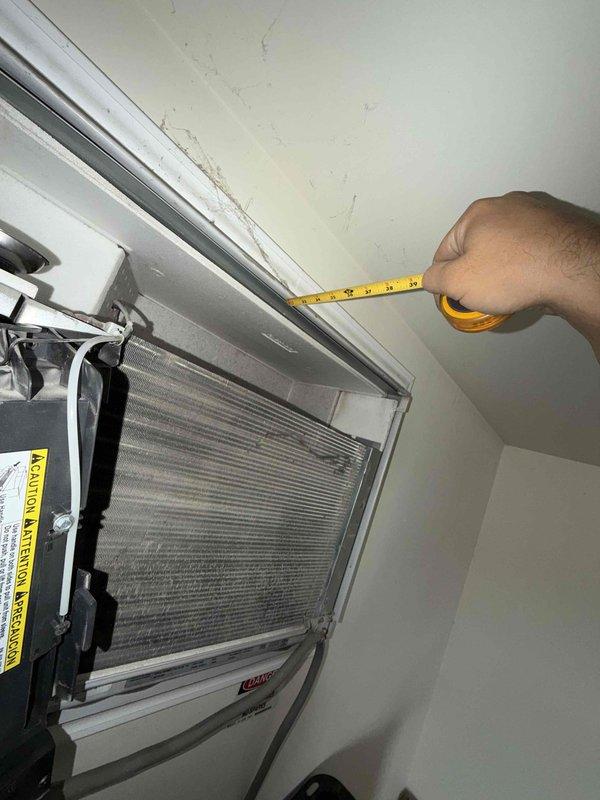 Returned to commercial location during morning timeframe as scheduled for continued diagnostics on wall-mounted air handler unit. Performed detailed measurements and clearance assessments of indoor HVAC equipment installation. Documented unit positioning relative to ceiling, measuring vertical clearance space above air handler. Inspected front panel access and internal components including filter and coil assembly. Evaluated mounting hardware and frame assembly at installation point, measuring gaps and checking foam insulation integrity at junction points. Photographed equipment condition, ceiling staining near unit, and installation specifications for further analysis and recommendation development.