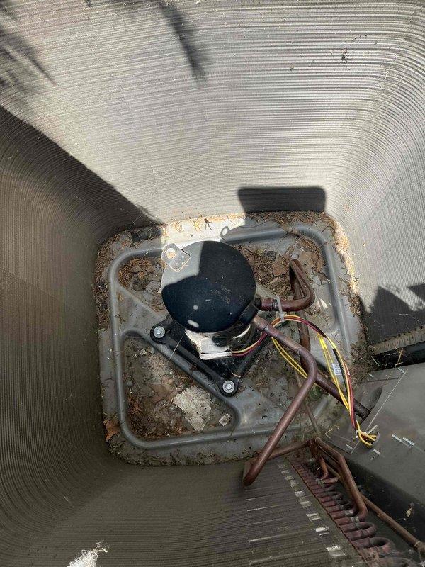 Completed comprehensive A/C tune-up on residential outdoor heat pump unit. Performed standard maintenance inspection of cylindrical condenser coils, blower motor assembly, and associated electrical connections. Noted visible corrosion on interior mounting pan and debris accumulation around blower motor base, though system remains operational. All wiring connections, copper refrigerant lines, and motor components inspected and confirmed secure. Unit operating within normal parameters following tune-up procedures.