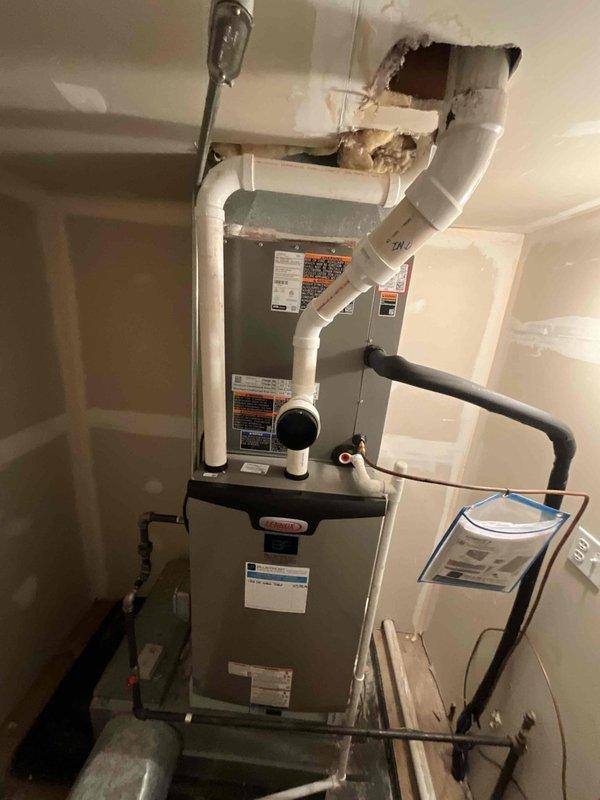 Responded to after hours service call for HVAC system not cooling properly. Upon arrival, found thermostat displaying indoor temperature of 79°F with setpoint at 72°F, indicating system was running but not achieving desired temperature. Inspected mechanical room and discovered furnace unit with significant ceiling damage above equipment, exposing interior structure with compromised drywall and visible backing material. Assessed white PVC vent piping connections running through damaged ceiling area to ensure proper exhaust ventilation remained intact. Verified all HVAC components, including furnace unit and adjacent water heater, were functioning safely despite structural damage to surrounding area. Advised that ceiling damage requires immediate attention to prevent further deterioration and potential impact on system ventilation, though HVAC equipment remains operational at this time.