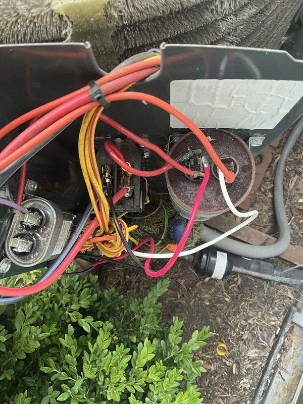 Responded to after hours service call for HVAC system malfunction. Upon arrival, inspected outdoor condensing unit and found electrical compartment accessible for diagnostics. Examined capacitor assembly and associated wiring connections, noting multiple color-coded electrical leads properly terminated to capacitor terminals. Verified all wire bundle connections secure with cable ties maintaining organized routing throughout electrical compartment. Inspected flexible ductwork connections at unit interface and confirmed proper seating. Evaluated indoor refrigerant line bundle routing through confined utility space, observing multiple service lines including supply, return, and drain configurations with brass fittings at connection points. All utility lines showed normal wear consistent with system age. Completed visual inspection of all accessible components, verified electrical connections tight, and confirmed system ready for operation. Unit returned to service.