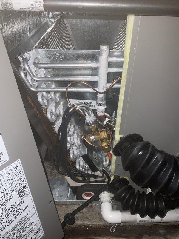 Responded to service call for newly installed Lennox furnace (Model GK40DT) with reported water leakage on floor and surrounding dampness. Upon arrival, unit was shut off by homeowner due to concerns about potential mold growth and lack of cooling on first floor while second floor maintained cold air. 

Performed diagnostic inspection and documented extensive condensation throughout the unit's internal components. Visual examination revealed significant moisture accumulation on copper refrigerant lines, compressor housing, and metallic surfaces within the air handler compartment. Water droplets were clearly visible coating refrigerant tubing and other components, indicating active condensation issues. Inspected white PVC condensate drainage system and verified proper installation of drain lines. 

Examined A2L refrigerant system specifications and confirmed unit is operating with appropriate safety classifications. Checked all accessible components including mesh filter, insulated copp