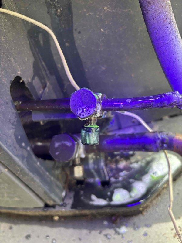 Technician returned to residential system to complete leak detection inspection using UV dye method. Upon inspection of the indoor unit, identified bright purple UV dye tracing visible on refrigerant lines, confirming active refrigerant leak at valve core location. Removed defective Schrader valve core from system, which showed signs of seal failure allowing refrigerant to escape. Leak source successfully located and documented with photographic evidence for repair recommendations.