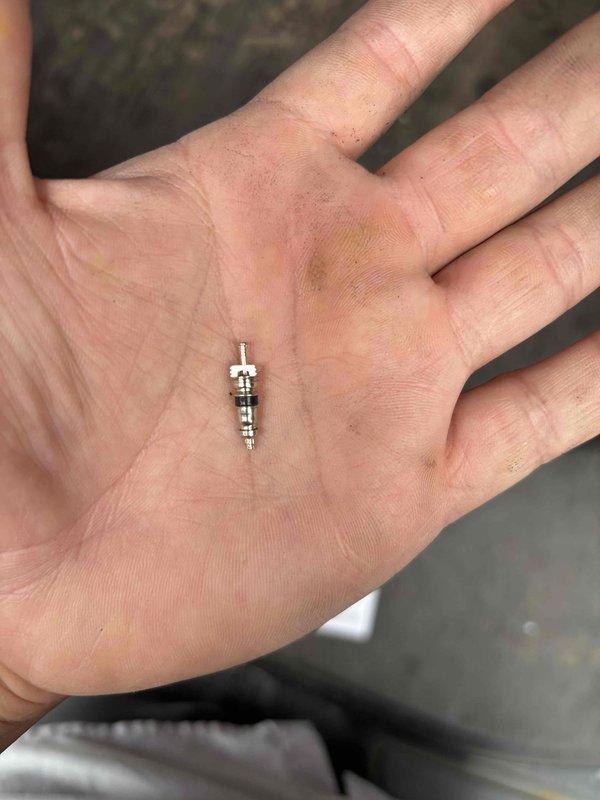 Technician returned to residential system to complete leak detection inspection using UV dye method. Upon inspection of the indoor unit, identified bright purple UV dye tracing visible on refrigerant lines, confirming active refrigerant leak at valve core location. Removed defective Schrader valve core from system, which showed signs of seal failure allowing refrigerant to escape. Leak source successfully located and documented with photographic evidence for repair recommendations.
