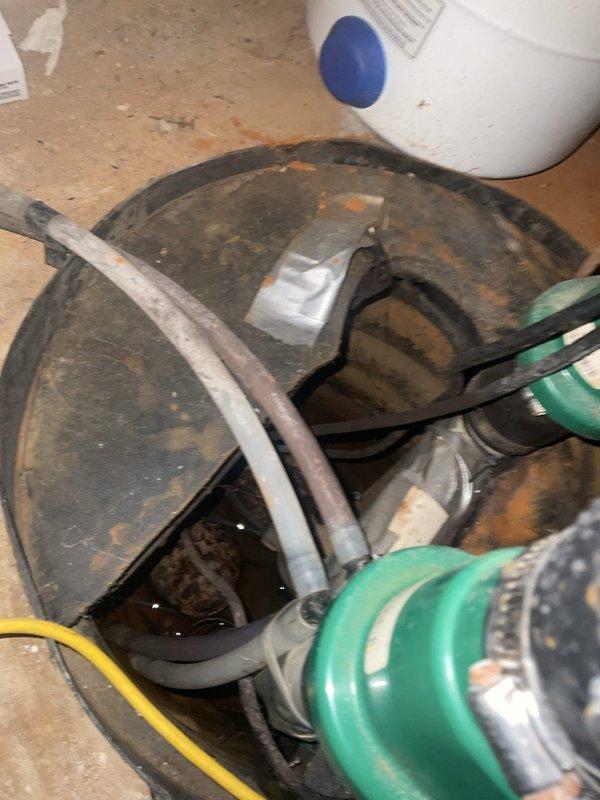 # Sump Pump Inspection

Performed comprehensive inspection of existing sump pump system in basement utility area. Examined primary sump pump assembly, including pump housing, motor, and discharge piping configuration. Noted significant accumulation of dirt, grime, and surface corrosion on pump housing, indicating extended service period. Verified proper connection of discharge hoses and electrical supply cord. Inspected auxiliary green pump component and associated plumbing connections for proper operation. Documented white PVC discharge piping routing and wall penetrations. Checked electrical connections including wall-mounted junction box and wiring integrity. Captured photographic documentation of pump condition and overall system configuration for service records. All components operational at time of inspection.