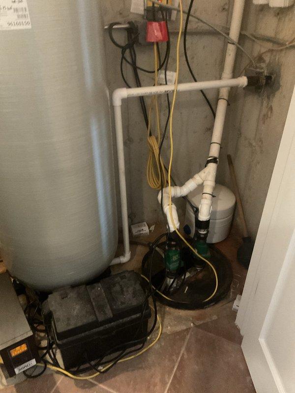 # Sump Pump Inspection

Performed comprehensive inspection of existing sump pump system in basement utility area. Examined primary sump pump assembly, including pump housing, motor, and discharge piping configuration. Noted significant accumulation of dirt, grime, and surface corrosion on pump housing, indicating extended service period. Verified proper connection of discharge hoses and electrical supply cord. Inspected auxiliary green pump component and associated plumbing connections for proper operation. Documented white PVC discharge piping routing and wall penetrations. Checked electrical connections including wall-mounted junction box and wiring integrity. Captured photographic documentation of pump condition and overall system configuration for service records. All components operational at time of inspection.