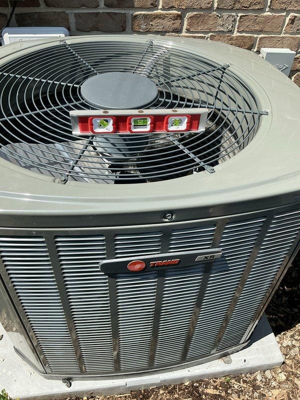 Leveled outdoor Trane air conditioning condenser unit that had settled unevenly on its concrete pad. Used precision level to verify proper horizontal alignment across multiple axes, ensuring optimal equipment operation and preventing future compressor damage or refrigerant migration issues. Unit was successfully adjusted and confirmed level for proper drainage and mechanical function.