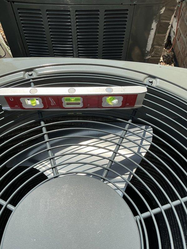 Leveled outdoor Trane air conditioning condenser unit that had settled unevenly on its concrete pad. Used precision level to verify proper horizontal alignment across multiple axes, ensuring optimal equipment operation and preventing future compressor damage or refrigerant migration issues. Unit was successfully adjusted and confirmed level for proper drainage and mechanical function.