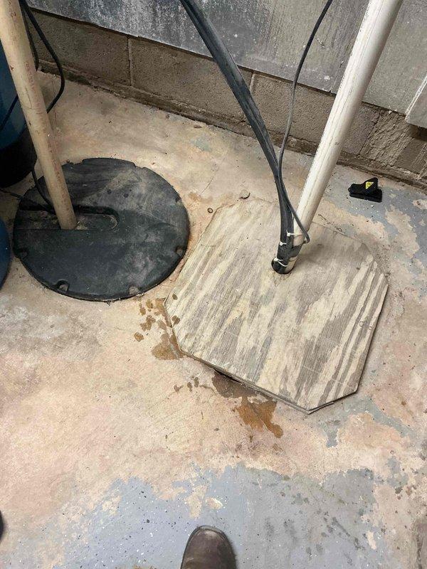 Completed comprehensive sump pump inspection in basement utility area as requested during morning hours. System evaluated including check valve operation, discharge piping, electrical connections, and sump pit condition. Floor area showed evidence of previous moisture accumulation near corner, indicating potential drainage concerns. Documented all components with photographs, verified proper installation of one-way check valve on discharge line, and assessed overall system functionality to ensure reliable operation during future water events.