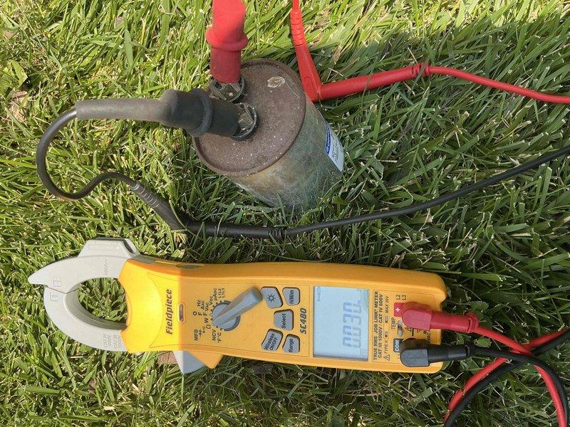 Responded to after-hours emergency call for non-cooling air conditioning system on approximately 60-year-old unit. Performed diagnostic evaluation of system components, documented equipment condition with photographs showing aged compressor assembly with weathered exterior casing and connected refrigerant lines, and measured electrical parameters using clamp meter which indicated no current draw, suggesting compressor failure or electrical disconnect.