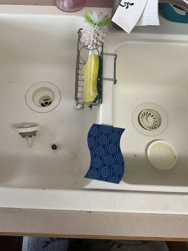 Responded to service call for water leak beneath kitchen sink at drain connection. Upon inspection, identified moisture accumulation in drip pan under cabinet, indicating active or recent leak at drain assembly. Inspected PVC P-trap and drain connections for proper seal and tightness. Addressed leak source at drain tailpiece connection point where drain exits sink basin. Tightened connections and verified proper seal at all drain assembly joints. Tested system for leaks by running water through both sink basins and monitoring drain connections for any signs of moisture. Confirmed repair successful with no active leaking observed. Cabinet interior and drip pan showed evidence of previous water exposure but no active water present after repair completion.