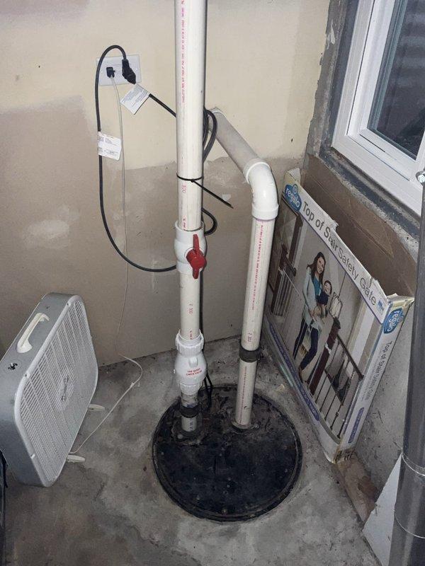 Responded to report of suspected ejector pump or sump pump leak in basement. Upon inspection, examined sump pump system with white PVC discharge piping, red valve assembly, and electrical connections. Verified sump pump basin installation and checked for signs of water intrusion or active leaking around pump components and discharge lines. Also inspected Rheem water heater in adjacent utility closet to rule out alternative water sources. Documented equipment conditions with photos for service records.