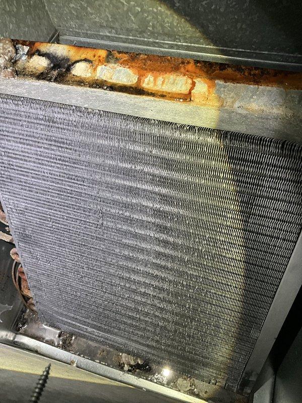 Responded to water leak in front of furnace. Upon arrival, found active water leakage and shut down unit for safety. Inspection revealed severely corroded evaporator coil with significant rust deterioration at top edge and mounting frame, along with corroded drain piping connections showing moisture streaking. Cleaned up standing water and documented extensive corrosion damage requiring coil replacement to prevent future leaks and restore proper system operation.