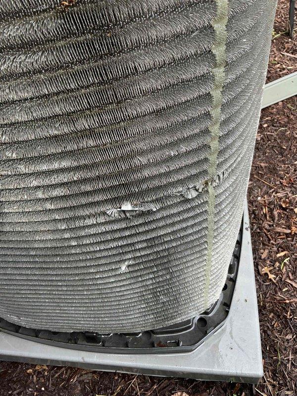 Completed comprehensive AC maintenance tune-up on residential outdoor condensing unit and inspected indoor thermostat system. Performed standard preventive maintenance procedures including coil inspection, system performance verification, and operational testing. Documented condenser coil condition showing environmental wear, surface discoloration, and section of damaged fins with compression affecting airflow efficiency in center-right quadrant of unit. Verified Honeywell Home ProSeries programmable thermostat operational and displaying proper temperature readings. System operational upon completion of maintenance service.