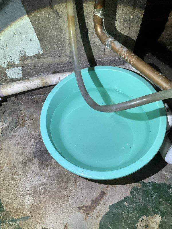 Responded to service call for leaking tankless water heater at residential property. Upon inspection, identified water leak originating from plumbing connections beneath the unit. Evaluated isolation valve assembly with red handle lever and associated brass compression fittings for signs of failure or loose connections. Assessed drainage collection system consisting of turquoise basin positioned on basement floor with rubber discharge tubes directing water away from the unit. Tightened compression fittings, inspected valve seals, and verified proper operation of shut-off valve to isolate the water heater for repair. Tested system for leaks after repairs and confirmed proper drainage function.
