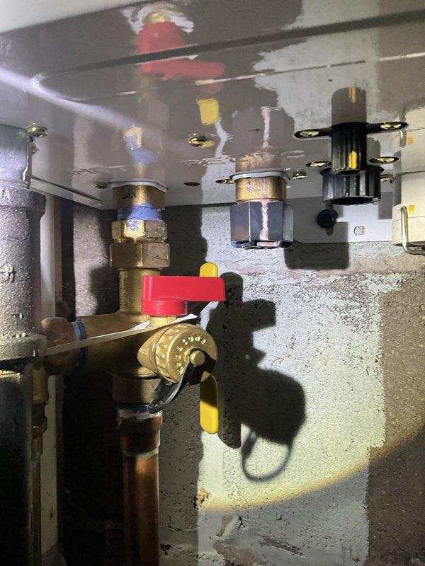 Responded to service call for leaking tankless water heater at residential property. Upon inspection, identified water leak originating from plumbing connections beneath the unit. Evaluated isolation valve assembly with red handle lever and associated brass compression fittings for signs of failure or loose connections. Assessed drainage collection system consisting of turquoise basin positioned on basement floor with rubber discharge tubes directing water away from the unit. Tightened compression fittings, inspected valve seals, and verified proper operation of shut-off valve to isolate the water heater for repair. Tested system for leaks after repairs and confirmed proper drainage function.