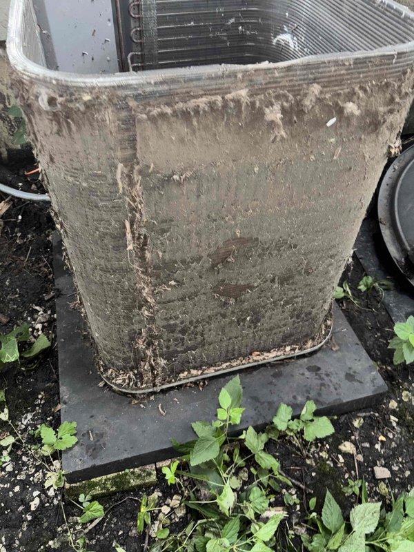 Completed comprehensive air conditioning tune-up on 9-10+ year old outdoor condensing unit. Upon arrival, found unit heavily soiled with accumulated dirt, debris, and biological growth on exterior casing and condenser coils, with vegetation growing around base. Performed complete system inspection, cleaned condenser coils and exterior surfaces, cleared debris from unit perimeter, tested electrical connections, verified refrigerant levels, and ensured proper system operation. Unit returned to optimal performance with improved airflow and efficiency.