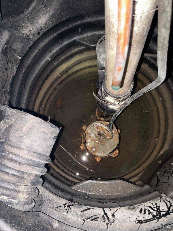 Completed comprehensive sump pump inspection in below-grade utility area. System evaluated included submersible pump unit with corrugated drainage inlet line and vertical discharge pipe showing rust staining on exterior surfaces. Pump housing, mounting hardware, and basin liner were inspected for proper operation and structural integrity. All components found functional with discharge piping secured by bracket assembly, though exterior corrosion noted on metal surfaces consistent with age and moisture exposure typical of below-grade water management installations.