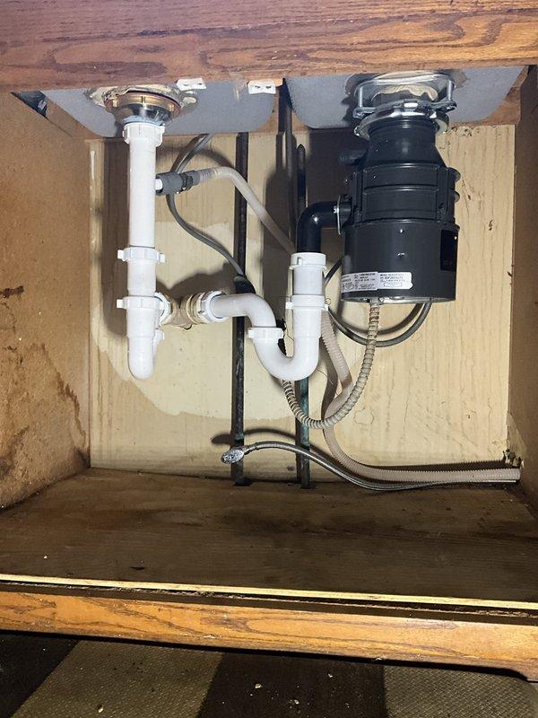 Removed and disposed of existing garbage disposal, basket strainer, and two p-traps from double-basin kitchen sink. Installed customer-provided garbage disposal unit on right side basin with electrical connection and mounted new basket strainer on left side basin. Completed installation with two new p-traps and dishwasher tailpiece, ensuring proper drainage configuration and secure connections throughout the system.