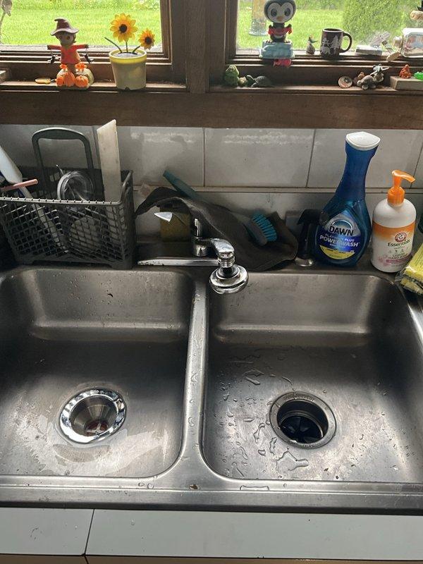 Removed and disposed of existing garbage disposal, basket strainer, and two p-traps from double-basin kitchen sink. Installed customer-provided garbage disposal unit on right side basin with electrical connection and mounted new basket strainer on left side basin. Completed installation with two new p-traps and dishwasher tailpiece, ensuring proper drainage configuration and secure connections throughout the system.