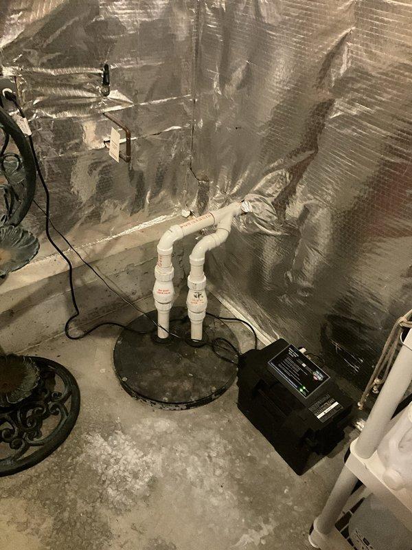 Completed comprehensive sump pump inspection in basement utility area. Verified proper operation of sump pump unit, checked discharge piping configuration including white PVC U-bend assembly, inspected pit condition and water level controls, and confirmed electrical connections were secure. All components found to be functioning within normal parameters with no immediate service needs identified.