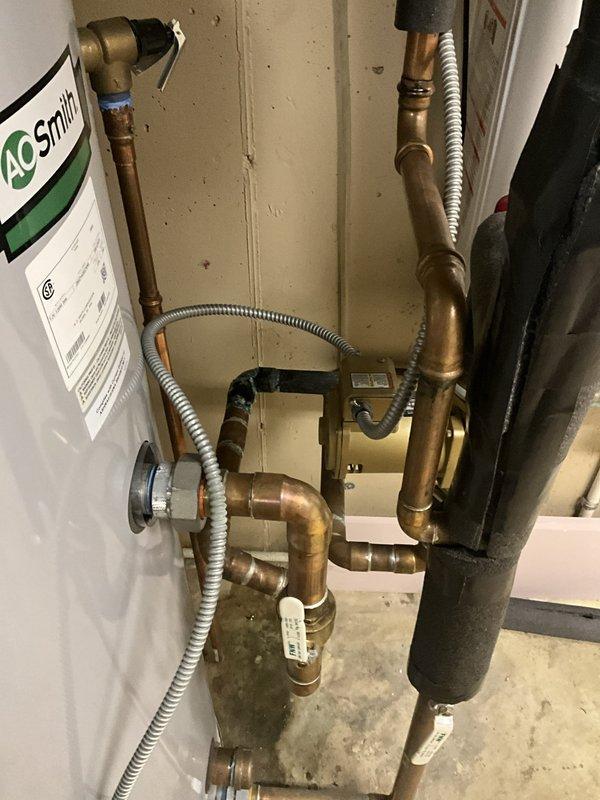Responded to no hot water complaint at commercial facility. Upon inspection, found deteriorated copper piping with significant corrosion and joint failure near the A.O. Smith tanked water heater system. Evidence of active water leakage was present on concrete floor beneath compromised piping connections. Assessed water heater components, circulation pump, and associated plumbing infrastructure. Documented existing conditions showing darkened deterioration at pipe joints and moisture damage indicating ongoing leak. System evaluated for proper operation and identified failed piping as primary cause of service interruption.